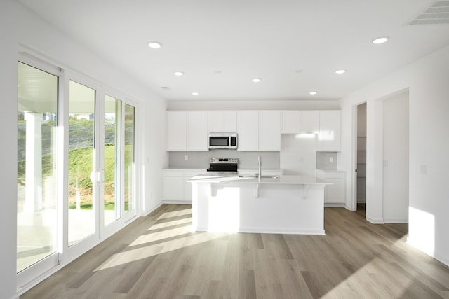 kitchen with light hardwood / wood-style flooring, a kitchen island with sink, stainless steel appliances, white cabinets, and a kitchen bar