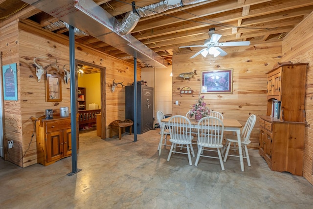 dining area featuring wooden walls, concrete floors, and ceiling fan