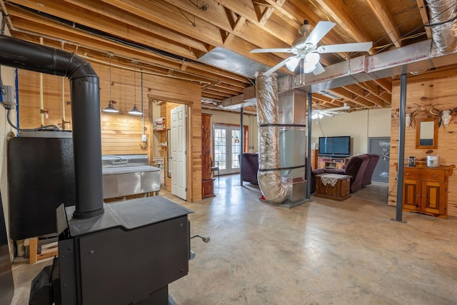 basement with ceiling fan, wooden walls, and a wood stove