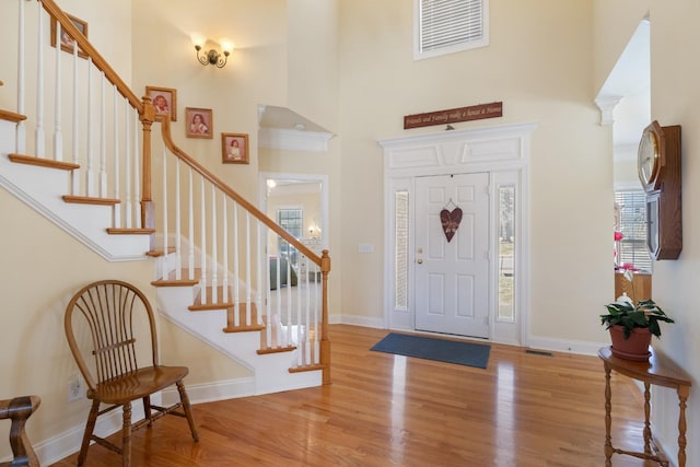 entryway with visible vents, a towering ceiling, baseboards, and wood finished floors