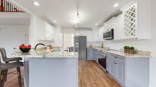 kitchen featuring a breakfast bar area, appliances with stainless steel finishes, hanging light fixtures, white cabinets, and kitchen peninsula