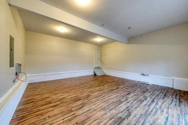 empty room featuring beam ceiling, an AC wall unit, electric panel, and light hardwood / wood-style floors