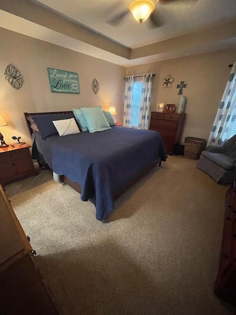 carpeted bedroom with ceiling fan and a raised ceiling