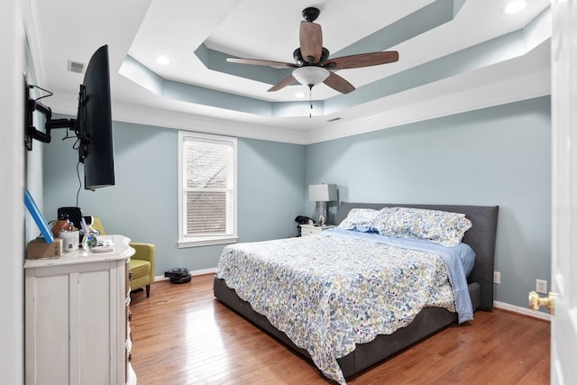 bedroom featuring hardwood / wood-style floors, a raised ceiling, and ceiling fan