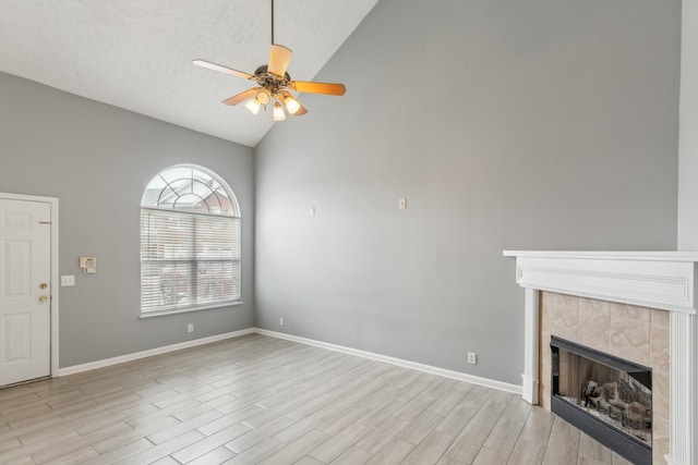 unfurnished living room with a tile fireplace, light wood-style flooring, a ceiling fan, baseboards, and vaulted ceiling