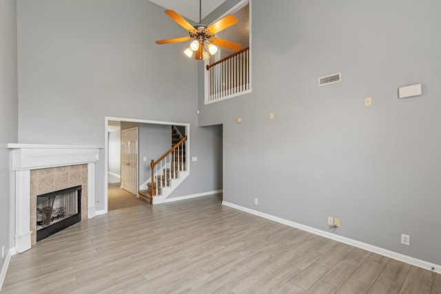 unfurnished living room featuring light wood finished floors, stairway, a tile fireplace, and visible vents