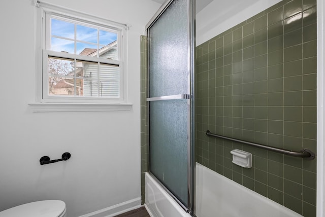 bathroom with toilet and bath / shower combo with glass door