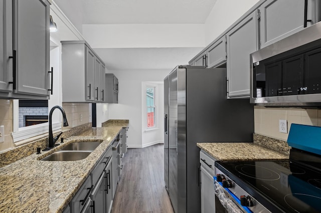 kitchen featuring dark wood-type flooring, sink, stainless steel appliances, light stone countertops, and backsplash