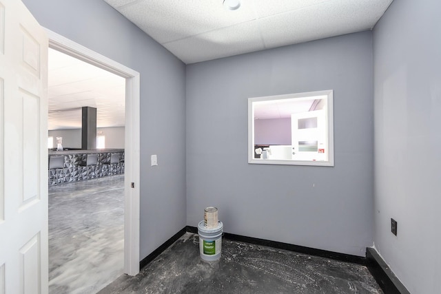 spare room with a drop ceiling, baseboards, and unfinished concrete floors