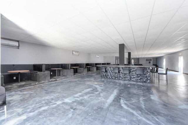 misc room featuring a drop ceiling, an AC wall unit, and concrete flooring