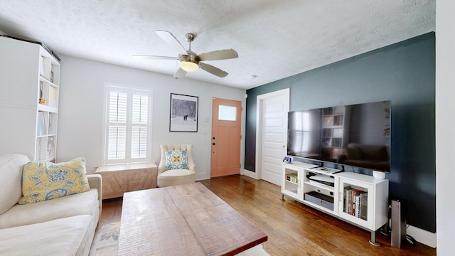 living room with a textured ceiling, ceiling fan, wood finished floors, and baseboards