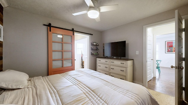 bedroom with a ceiling fan, wood finished floors, a textured ceiling, and a barn door