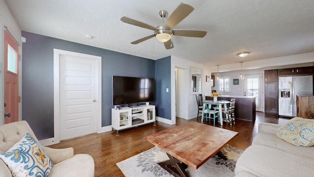 living room with dark wood-style floors, ceiling fan, and baseboards