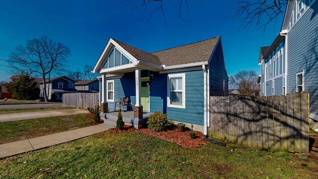 view of front of house featuring a front yard, covered porch, roof with shingles, and fence