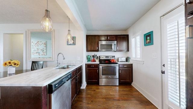 kitchen featuring appliances with stainless steel finishes, dark wood-style flooring, light countertops, pendant lighting, and a sink