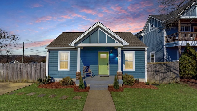 bungalow-style house featuring roof with shingles, fence, and a lawn