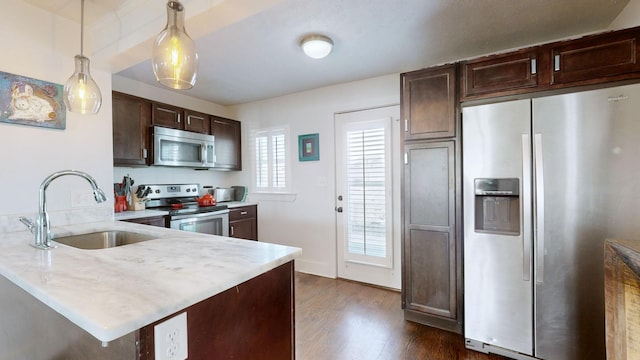 kitchen featuring stainless steel appliances, a peninsula, a sink, light countertops, and pendant lighting