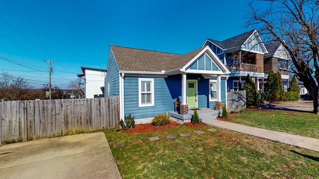 view of front of house featuring roof with shingles, a front yard, fence, and a balcony