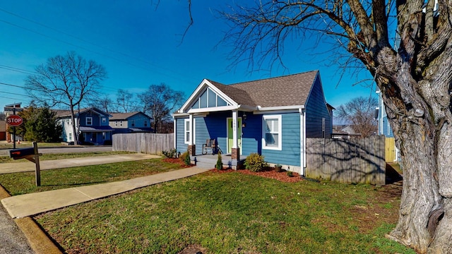 bungalow with a shingled roof, fence, and a front lawn