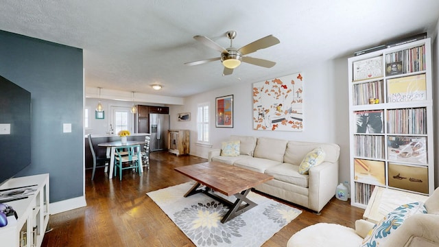 living area with dark wood-style floors, a textured ceiling, baseboards, and a ceiling fan