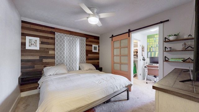 bedroom featuring ceiling fan, light carpet, wood walls, and a barn door