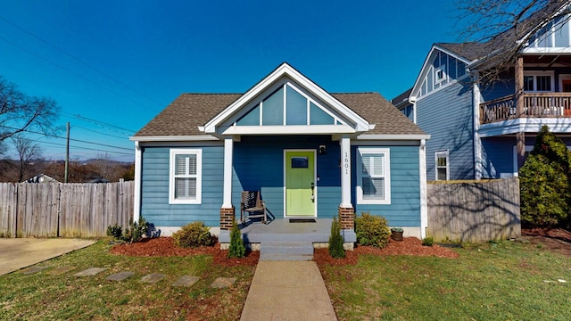 bungalow with a front yard, covered porch, roof with shingles, and fence