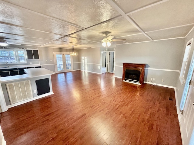 unfurnished living room with wood-type flooring, coffered ceiling, ceiling fan with notable chandelier, and a textured ceiling