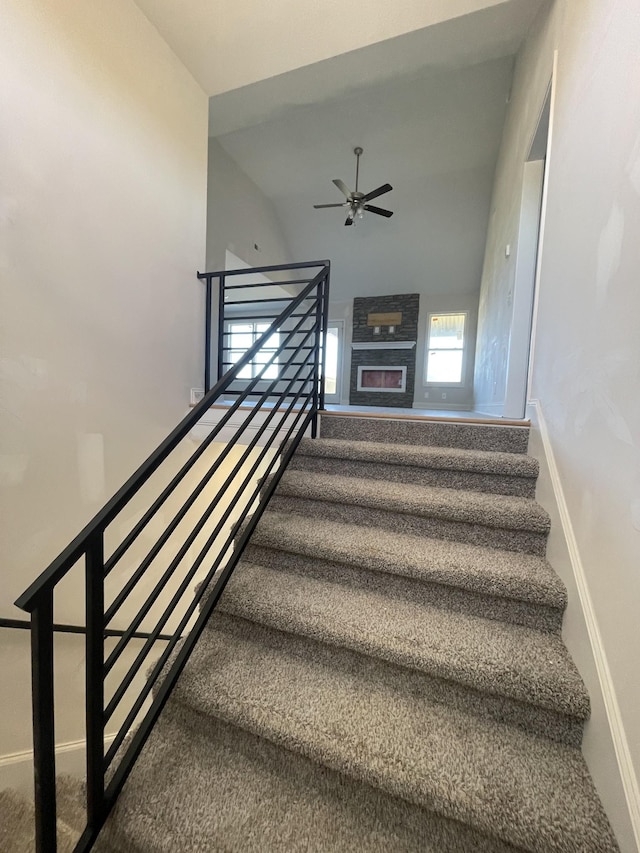 stairway with a stone fireplace and ceiling fan