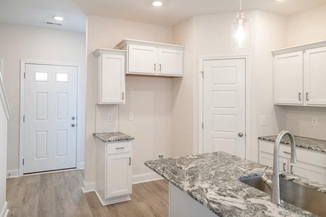 kitchen featuring sink, light stone counters, white cabinets, decorative light fixtures, and light wood-type flooring