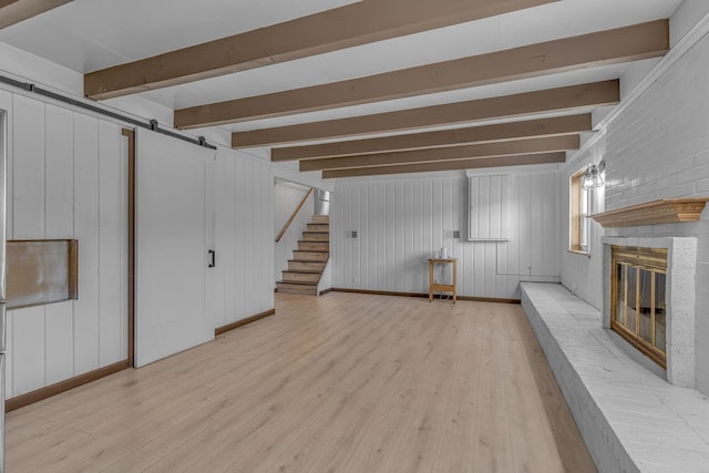 basement with a fireplace, a barn door, and light hardwood / wood-style flooring
