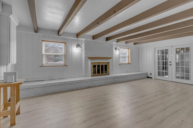 unfurnished living room with beam ceiling, a fireplace, light wood-type flooring, and french doors