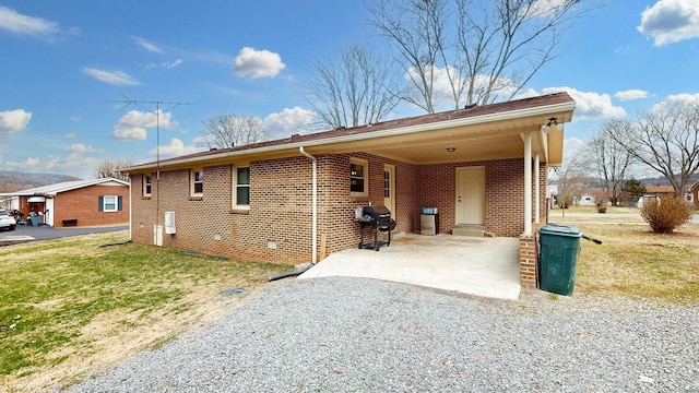 view of side of home featuring an attached carport, brick siding, driveway, and a lawn