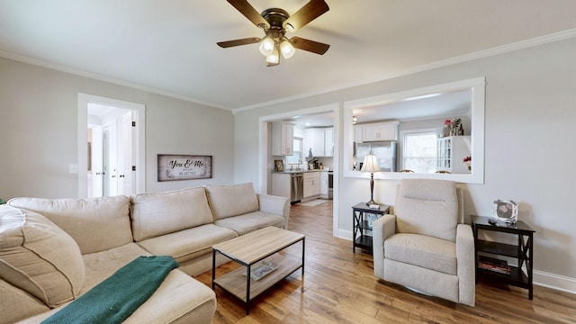 living area with crown molding, ceiling fan, baseboards, and light wood-style floors