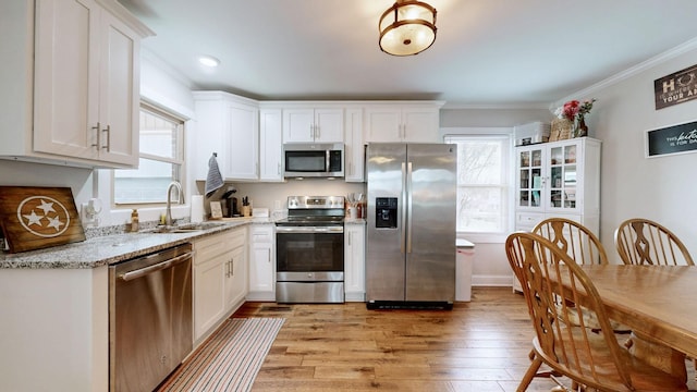 kitchen with appliances with stainless steel finishes, white cabinetry, light wood-style flooring, and light stone counters