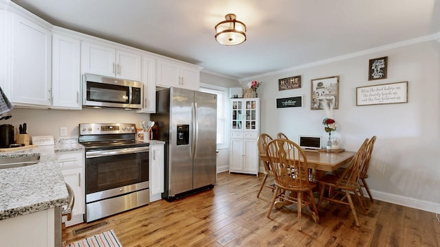 kitchen with light wood-style flooring, appliances with stainless steel finishes, light stone counters, crown molding, and white cabinetry