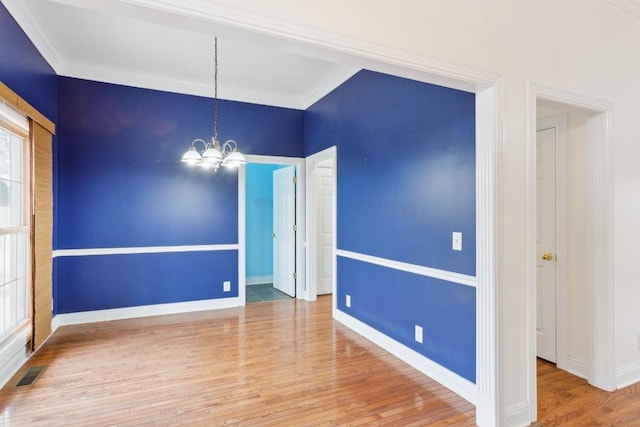 spare room with visible vents, baseboards, ornamental molding, an inviting chandelier, and wood finished floors