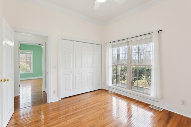 unfurnished bedroom with visible vents, baseboards, ornamental molding, light wood-style floors, and a closet
