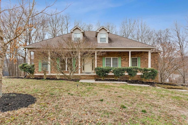 view of front of property with brick siding, covered porch, a front yard, and roof with shingles
