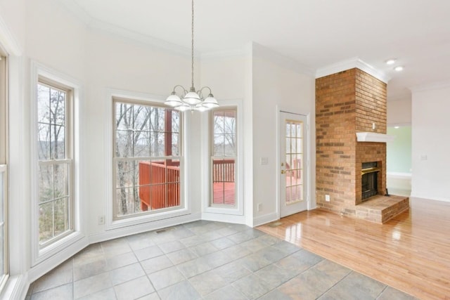 unfurnished dining area featuring a brick fireplace, crown molding, baseboards, a chandelier, and wood finished floors