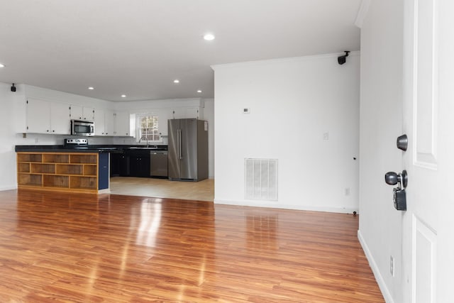 kitchen with stainless steel appliances, ornamental molding, white cabinets, and light hardwood / wood-style flooring