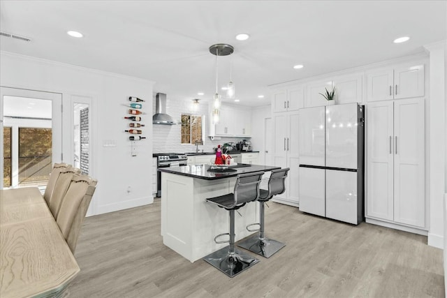 kitchen featuring wall chimney range hood, hanging light fixtures, stainless steel range oven, white cabinets, and white fridge