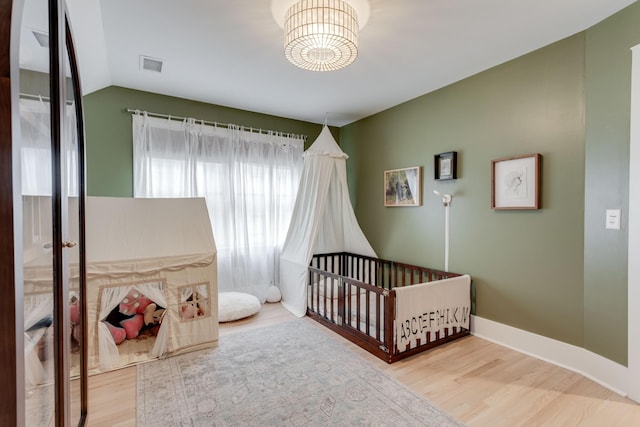 bedroom with a nursery area, lofted ceiling, a chandelier, and hardwood / wood-style floors