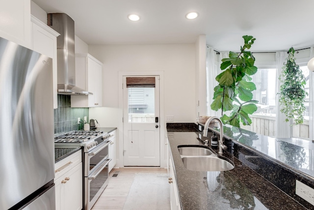 kitchen featuring stainless steel appliances, white cabinetry, sink, and wall chimney range hood