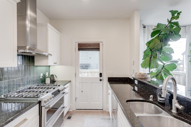 kitchen featuring range with two ovens, white cabinetry, sink, and wall chimney range hood