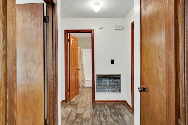 hall featuring wood-type flooring, heating unit, and a textured ceiling