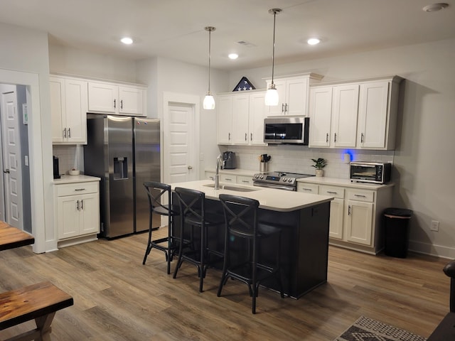 kitchen featuring appliances with stainless steel finishes, pendant lighting, white cabinetry, sink, and a center island with sink