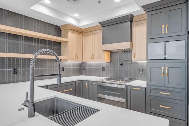 kitchen featuring gray cabinets, sink, range with two ovens, custom exhaust hood, and a raised ceiling