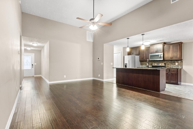 kitchen featuring dark hardwood / wood-style flooring, decorative backsplash, an island with sink, and appliances with stainless steel finishes