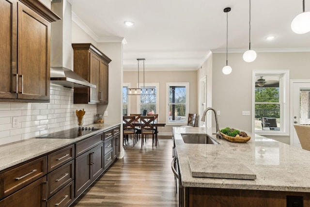 kitchen featuring an island with sink, hanging light fixtures, sink, black electric stovetop, and wall chimney exhaust hood