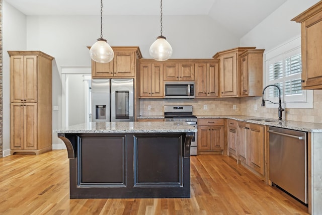 kitchen with sink, appliances with stainless steel finishes, hanging light fixtures, light stone countertops, and a kitchen island